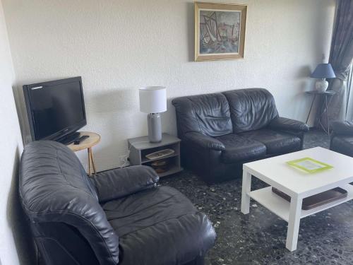 Il comprend un salon doté d'un mobilier en cuir noir et d'une télévision. dans l'établissement Appartement face mer climatisé avec parking au Grau-du-Roi - FR-1-731-141, au Grau-du-Roi