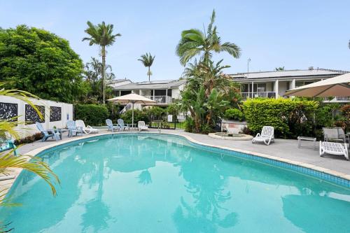 a swimming pool with chairs and trees and a building at Noosa Keys Apartments in Noosaville