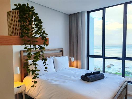 Un dormitorio con una cama blanca con una ventana grande. en Wavescape Endless Ocean, en Muizenberg