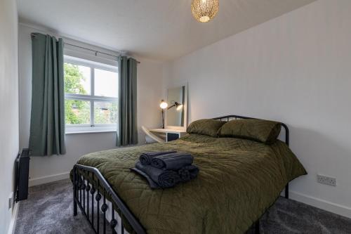 a bedroom with a bed with a green blanket and a window at Countryside Stay Near JCB, Peaks & Alton Towers in Rocester