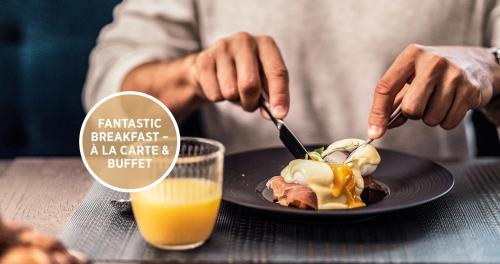 a person eating a dessert on a plate with a glass of orange juice at Falkensteiner Boutique Hotel Prague in Prague