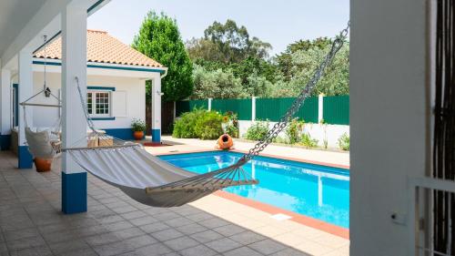 a hammock in front of a house with a pool at Villa Rio in Praia do Ribatejo