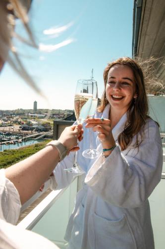a woman holding a glass of wine on a balcony at WestCord Hotel Schylge in West-Terschelling