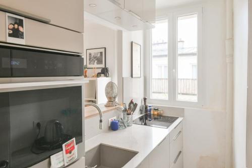 une cuisine blanche avec un évier et un micro-ondes dans l'établissement Appartement lumineux à Paris by Weekome, à Paris
