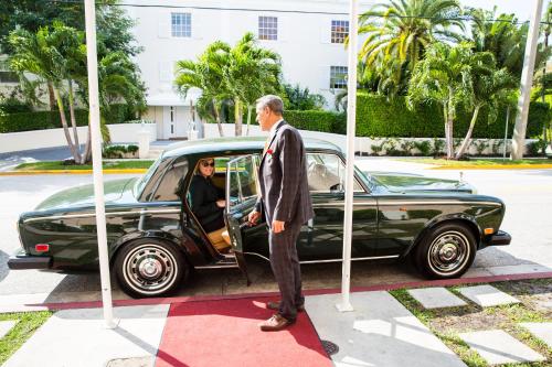 a man in a suit and tie standing next to a car at The Chesterfield Hotel Palm Beach in Palm Beach