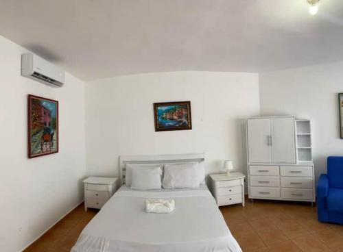 a white bedroom with a bed and a blue chair at Appartamento Albatros, Juan Dolio in Juan Dolio