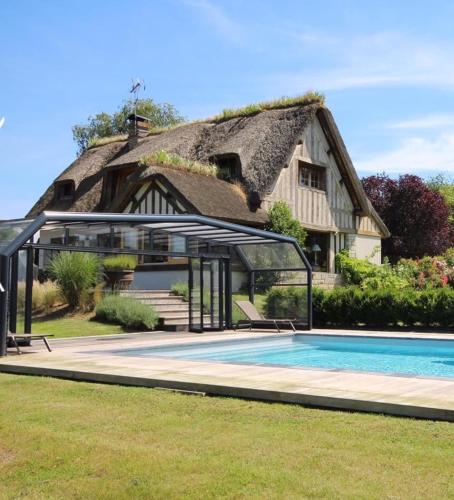 une maison avec un toit de chaume et une piscine dans l'établissement Chaumière de charme avec piscine, à Tourgéville