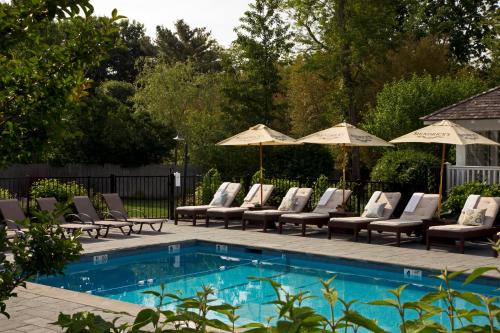 a swimming pool with lounge chairs and umbrellas at Shelter Island House in Shelter Island Heights