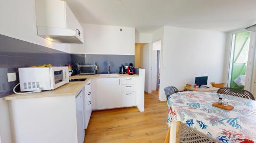 une cuisine avec des armoires blanches et une table avec un micro-ondes dans l'établissement Le Nid de la Mouette, à Saint-Hilaire-de-Riez