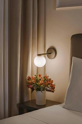 a lamp and a vase with flowers on a table next to a bed at Missori Hotel Piazza Missori, Sonder by Marriott Bonvoy in Milan