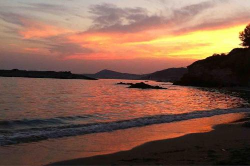 a sunset on a beach with the ocean and rocks at Agia Marina House, walking distance to the beach in Aghia Marina