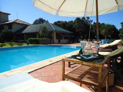 a table with glasses and an umbrella next to a swimming pool at Visconte Ditalia Hotel e Eventos in Nova Hartz
