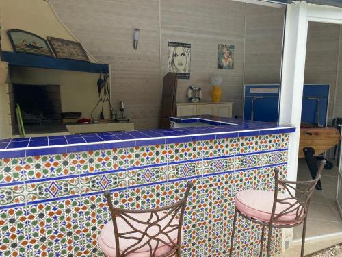 une cuisine avec un comptoir en carrelage coloré avec deux chaises dans l'établissement Les Oliviers, à Villemoustaussou