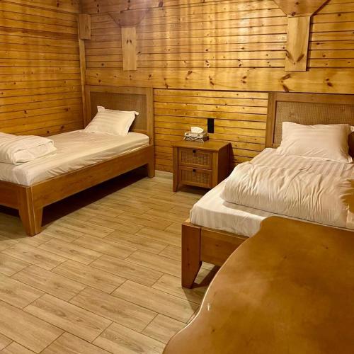 two beds in a room with wooden walls at أكواخ القرية -VILLAGE HUTs in Taif
