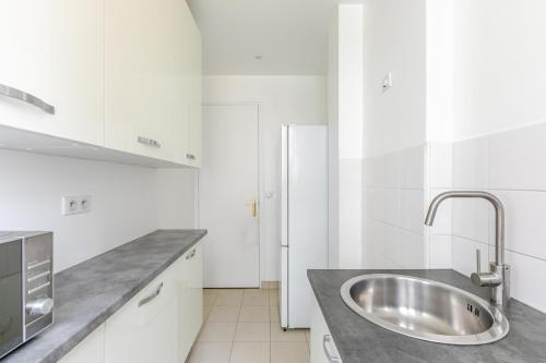 La cuisine blanche est équipée d'un évier et d'un réfrigérateur. dans l'établissement Appartement Neuilly Chic, Vivez l'Élégance - II, à Neuilly-sur-Seine