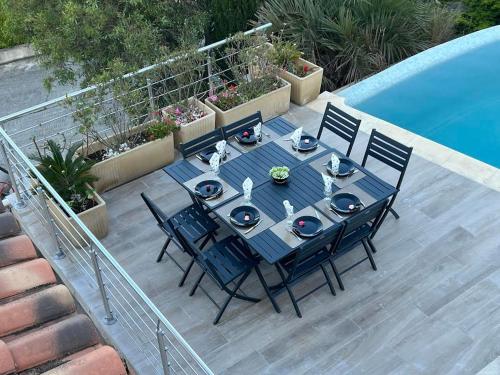 une table à manger et des chaises assises à côté d'une piscine dans l'établissement Les hauts d'Ou Souleou, villa contemporaine 8 personnes, piscine à débordement, jacuzzi intégré, très belle vue mer et collines, à Bormes-les-Mimosas