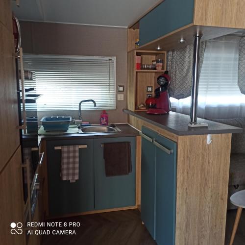 Elle comprend une petite cuisine avec des placards bleus et un évier. dans l'établissement Résidence Camping Les Dunes, au Grau-dʼAgde