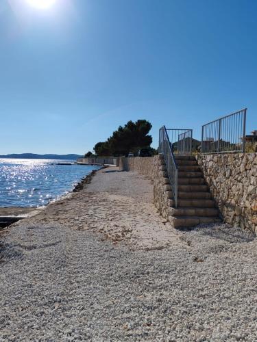 a beach with a stone wall and stairs next to the water at Seaside Serenity "Sea" with pool, 150m from sea in Sukošan