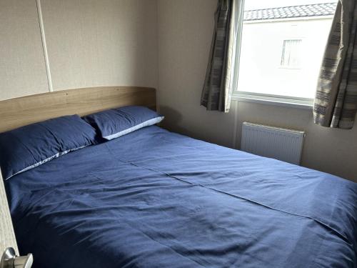 a bed with blue sheets in a bedroom with a window at A13 - Beach Haven at Silversands in Lossiemouth