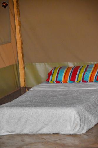 a bed with white sheets and colorful pillows at Oldonyo Musa Amboseli Campsite in Rift Valley