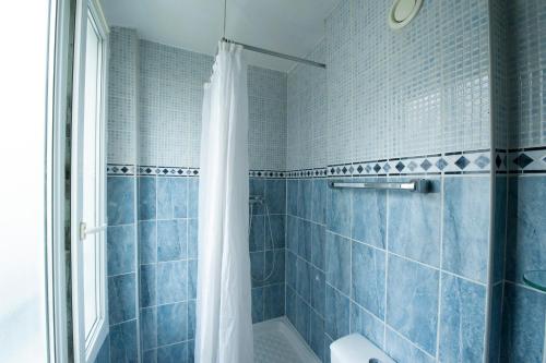 uma casa de banho com azulejos azuis e um chuveiro com uma cortina de chuveiro. em Hotel du Globe 18 em Paris