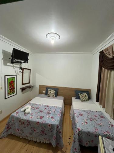 a bedroom with two beds and a tv on the wall at Hotel Ipê in São Luís Gonzaga
