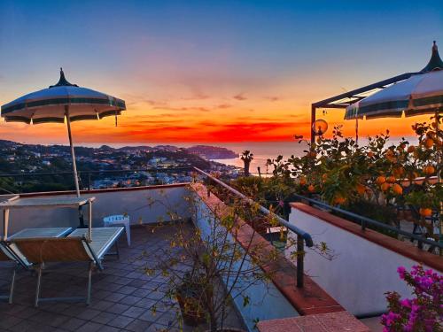 a view of a sunset from a balcony with chairs and an umbrella at Hotel Ape Regina in Ischia
