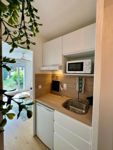 une cuisine avec un évier et un micro-ondes dans l'établissement Studio confort & calme avec piscine, à Mérignac
