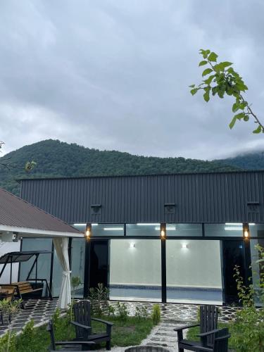a house with a glass facade with mountains in the background at Qafqaz Milan Villa With Outdoor Heated Pool in Gabala