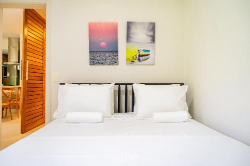 a bedroom with a white bed with three pictures on the wall at Apartamento em Cotovelo In Mare Bali 256 - Qavi in Granja Beira Mar