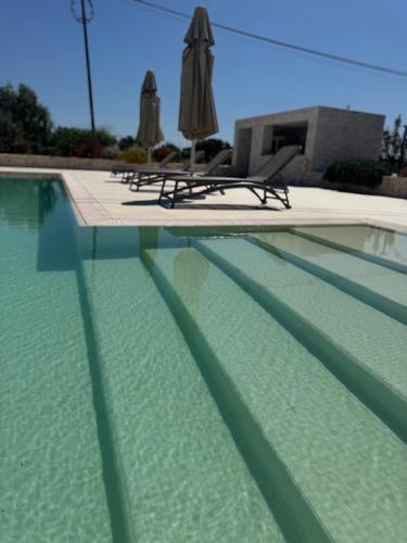 a swimming pool with two chairs and an umbrella at IL CARRUBO La dimora in Monopoli