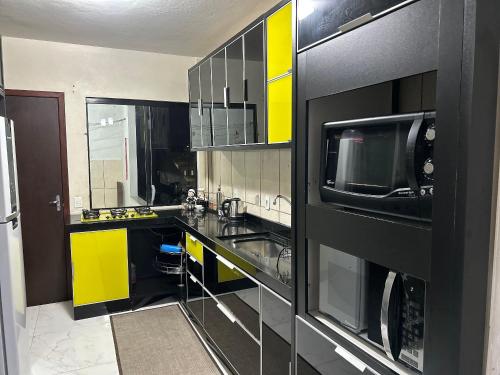 a kitchen with yellow and black cabinets and a microwave at Apartamento Aconchegante Central (Borboleta) in Itajaí