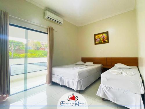 two beds in a room with a large window at Hotel Estação de Minas in Aparecida