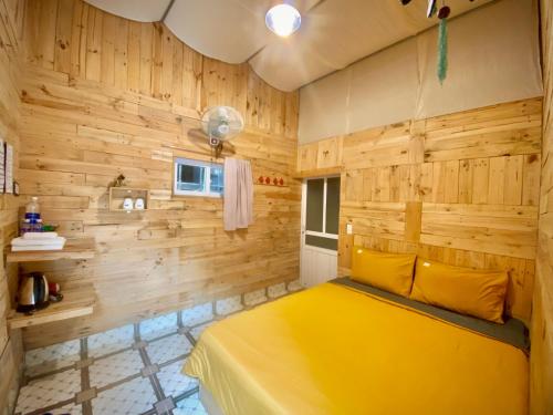 a yellow bed in a room with wooden walls at Homestay Gấu Smile - Mộc Châu in Sơn La