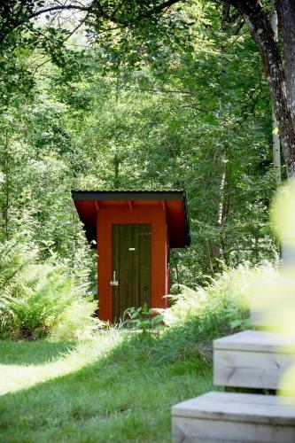 a red out house in the middle of a forest at Small Cabin With Outdoor Kitchen By Forest Stream in Trollhättan