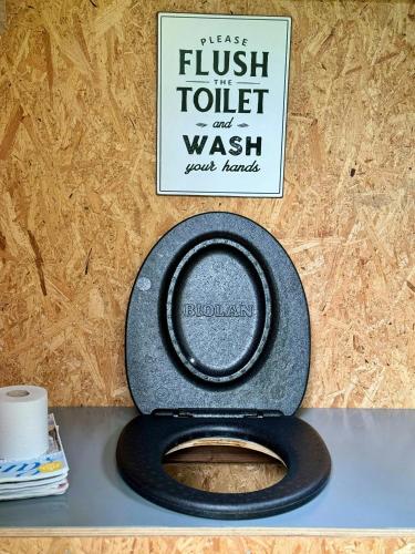 a toilet with a black seat and a sign on a wall at Small Cabin With Outdoor Kitchen By Forest Stream in Trollhättan