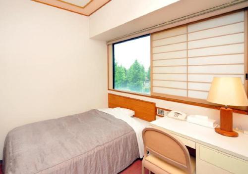 a bedroom with a bed and a desk and a window at Hotel Grand Shinonome in Tsukuba