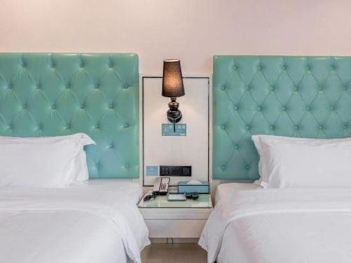 a bedroom with two beds and a green headboard at Xana Lite Anqing Yuexi Swan Squre Branch in Yuexi