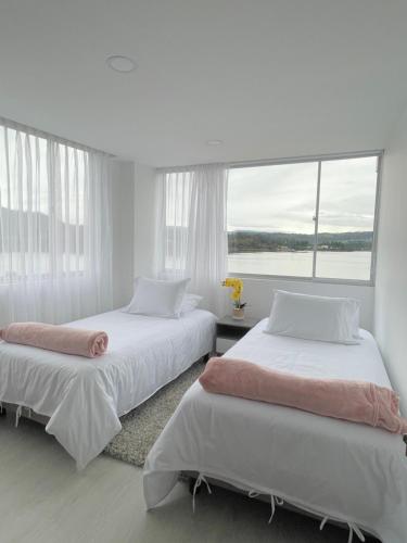 Dos camas en una habitación blanca con ventana. en Hermoso Apartamento con Vista al Lago, en Paipa