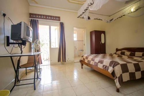 a bedroom with a bed and a desk with a television at Golden Tripod Hotel in Tororo
