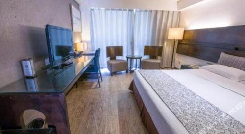 a hotel room with a bed and a desk with a television at Tianjin Juchuan Lily Hotel in Binhai