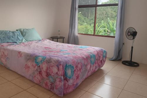 a bedroom with a bed with a pink floral bedspread and a window at Casa Rural Arturo in Cariari