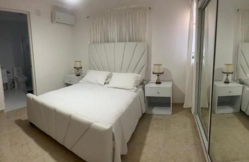 une chambre blanche avec un grand lit et un miroir dans l'établissement Casa de tres habitaciones con piscina, à La Romana