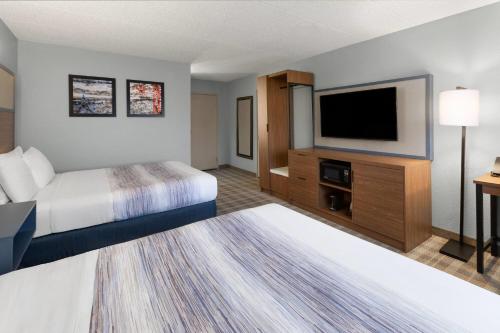 a hotel room with two beds and a flat screen tv at AmericInn by Wyndham Chippewa Falls in Chippewa Falls