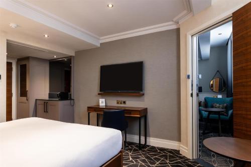 a hotel room with a bed and a desk and a television at 100 Queen's Gate Hotel London Kensington, Curio Collection by Hilton in London