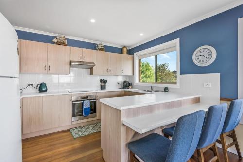 a kitchen with blue walls and a counter with blue chairs at Seascape Retreat at Bonny Hills in Bonny Hills