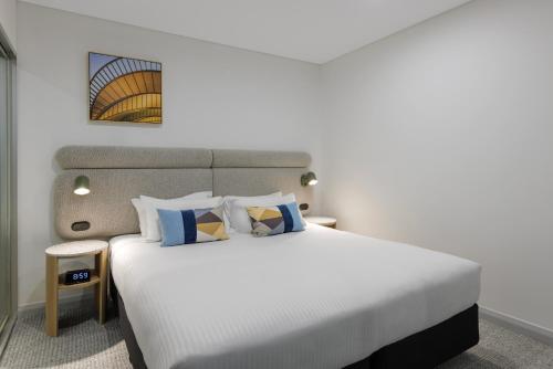 a bedroom with a white bed with blue and yellow pillows at Quest at Sydney Olympic Park in Sydney