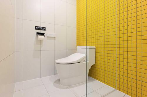 a bathroom with a toilet and a yellow tile wall at Moor Hotel Mokpo By Aank in Mokpo
