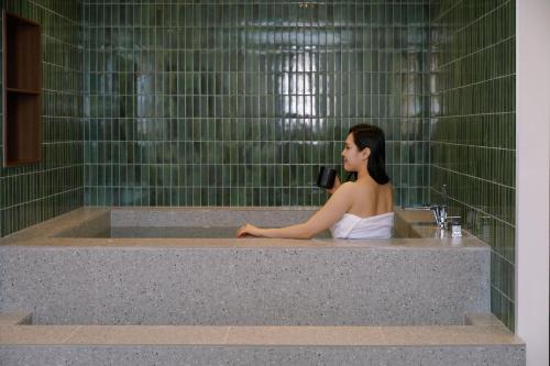 a woman sitting in a bath tub with a blow dryer at Moor Hotel Mokpo By Aank in Mokpo
