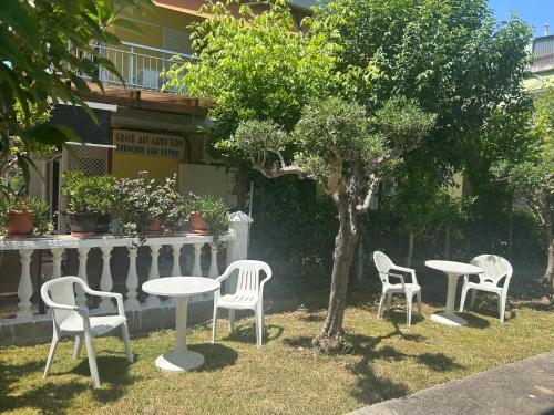 a group of white tables and chairs next to a tree at Dionisos Roses in Paralia Dionysiou